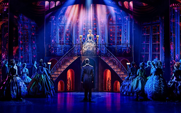 Cinderella on stage at Madrid theater, standing on staircase, surrounded by cast in elegant costumes.