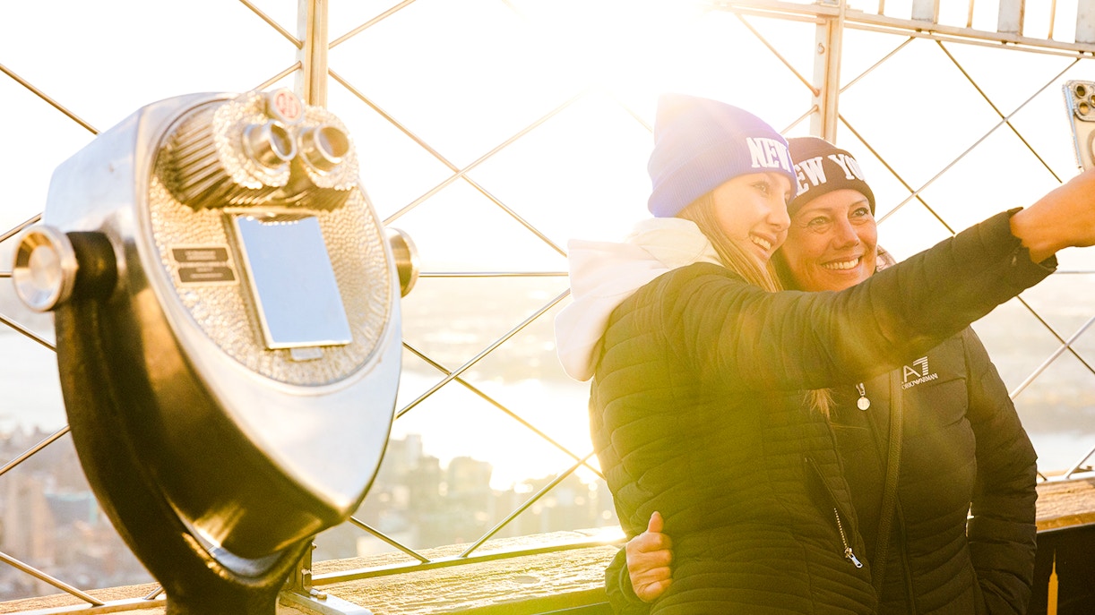Guests taking a selfie on the Empire State Building's observation deck with a viewfinder nearby.