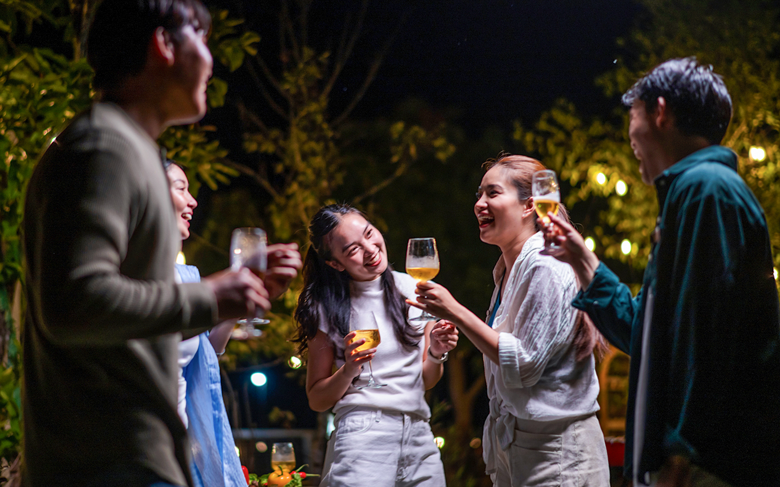 A group of people are gathered around a table, laughing and drinking wine