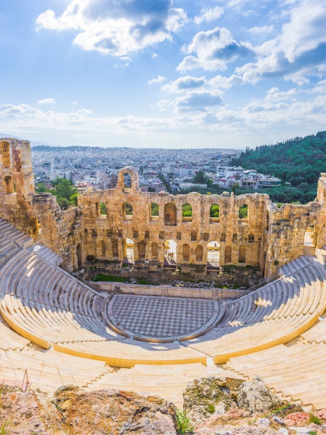 Ancient amphitheater in Athens with cityscape and hills in the background.