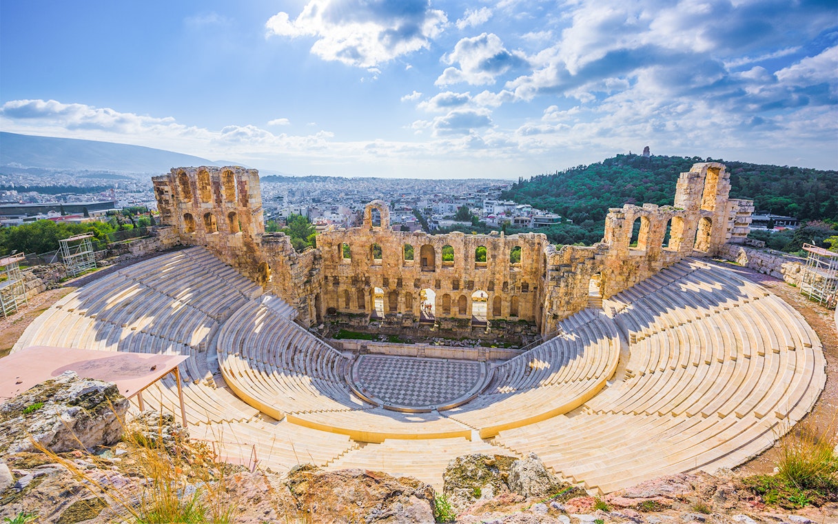 Ancient amphitheater in Athens with cityscape and hills in the background.
