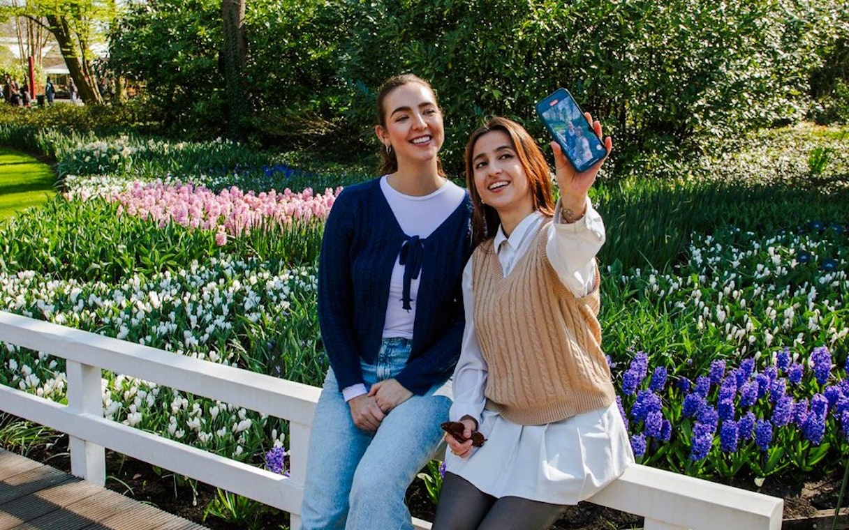 Visitors taking a selfie at Keukenhof Gardens, Amsterdam, with colorful tulip beds in the background.