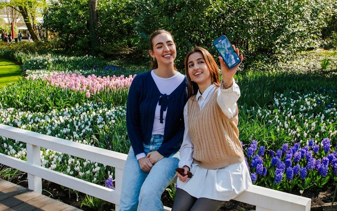 Visitors taking a selfie at Keukenhof Gardens, Amsterdam, with colorful tulip beds in the background.
