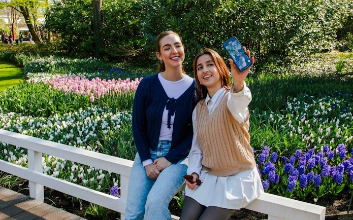 Visitors taking a selfie at Keukenhof Gardens, Amsterdam, with colorful tulip beds in the background.