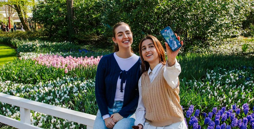 Visitors taking a selfie at Keukenhof Gardens, Amsterdam, with colorful tulip beds in the background.