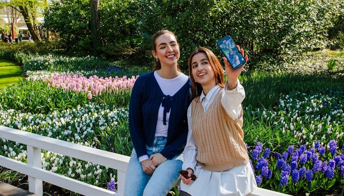 Visitors taking a selfie at Keukenhof Gardens, Amsterdam, with colorful tulip beds in the background.