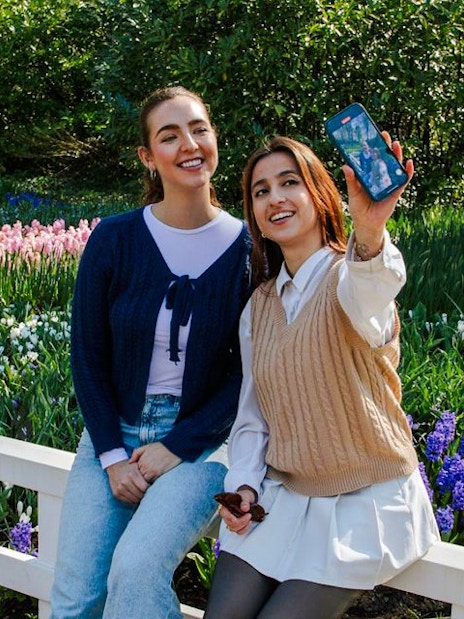 Visitors taking a selfie at Keukenhof Gardens, Amsterdam, with colorful tulip beds in the background.