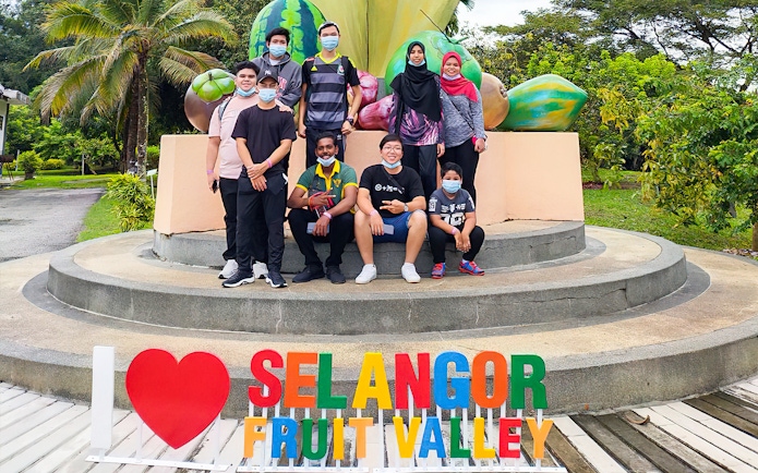 Group posing by Selangor Fruit Valley sign with fruit sculptures in the background.