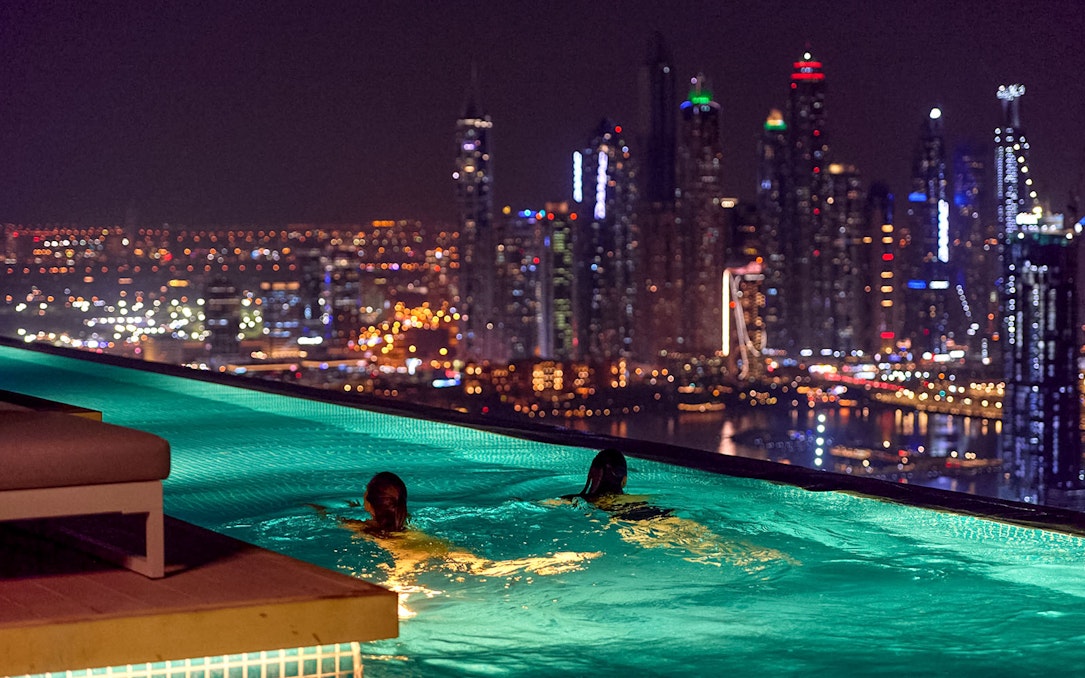 Tourists swimming at Aura Sky Pool with Dubai skyline at night.