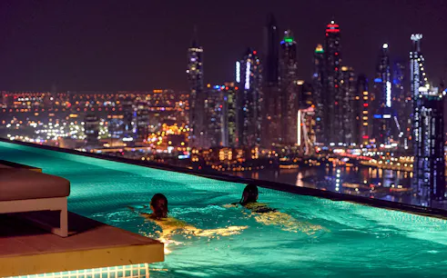 Tourists swimming at Aura Sky Pool with Dubai skyline at night.