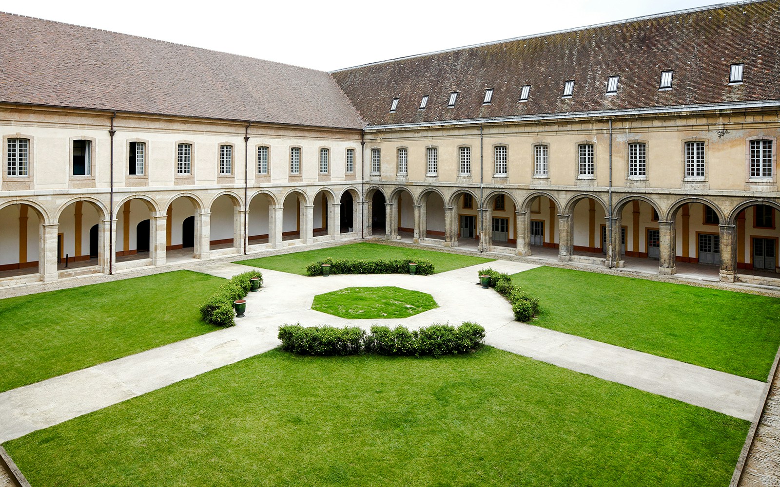 Cloister courtyard of Abbaye de Cluny in Lyon, France, featuring arched walkways and manicured lawns.