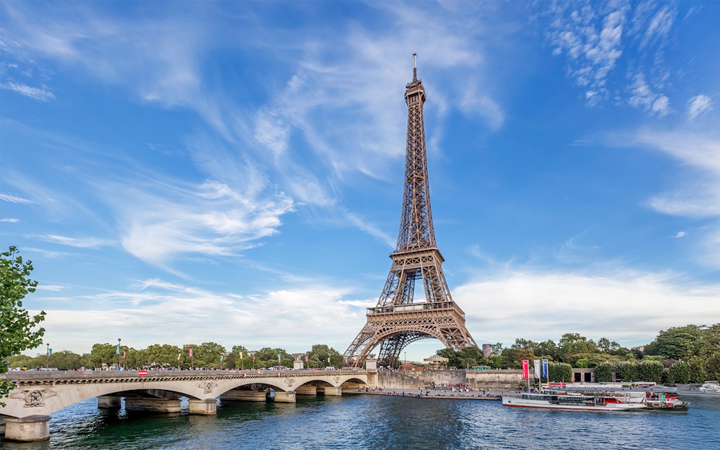 Eiffel Tower view from across the Seine River in Paris, with a boat passing by.
