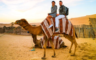 Couple on camel during Doha Desert safari at sunset.