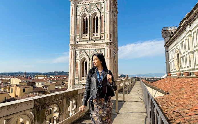 Tourist walking on Florence Duomo terrace with Giotto's Campanile in view.
