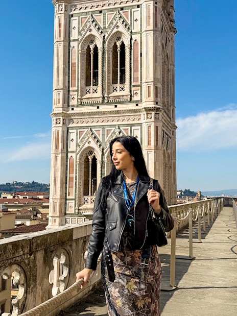 Tourist walking on Florence Duomo terrace with Giotto's Campanile in view.