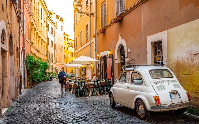 Cobblestone street in Rome with outdoor café and vintage car.