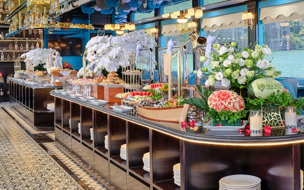Buffet table with fresh fruits, pastries, and floral arrangements on a cruise ship.