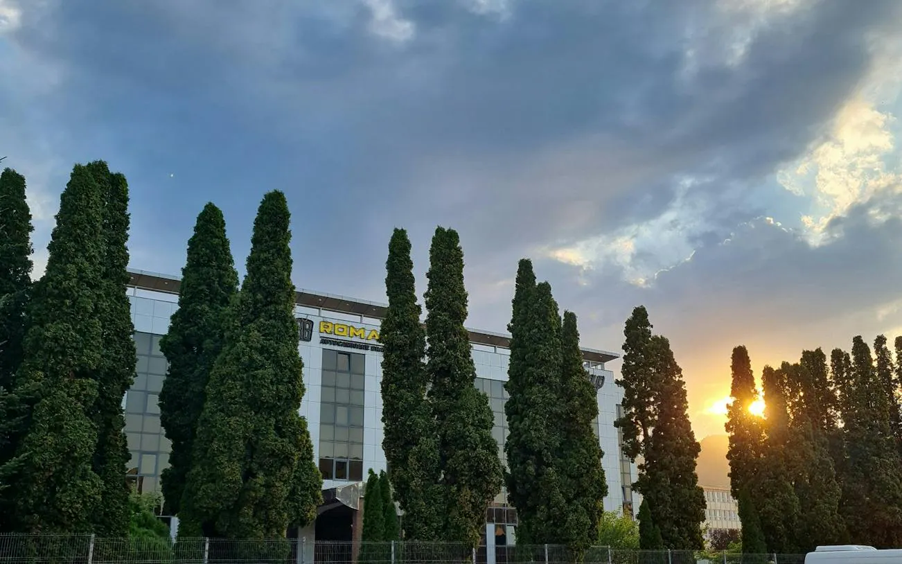 Building with tall trees at sunset, Brașov Workers' Protest 1987 exploration game location.