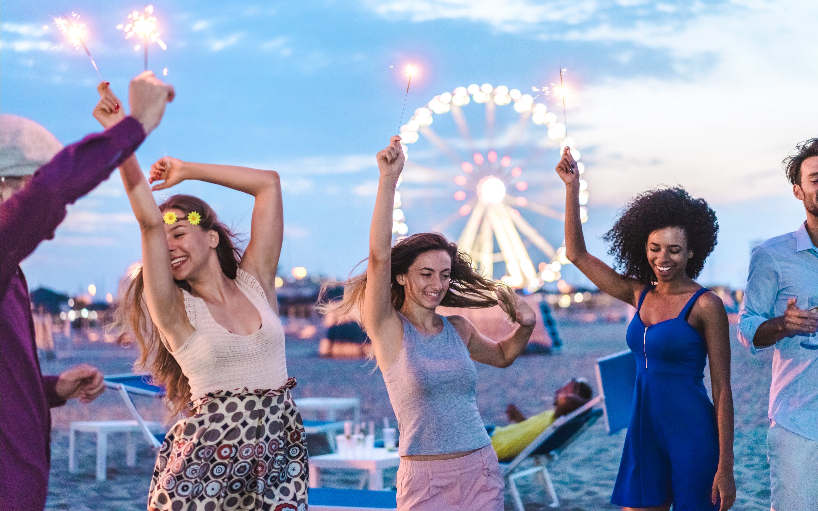 Friends celebrating with sparklers on a Miami beach at night, Ferris wheel in background.