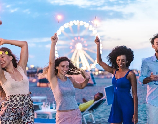 Friends celebrating with sparklers on a Miami beach at night, Ferris wheel in background.