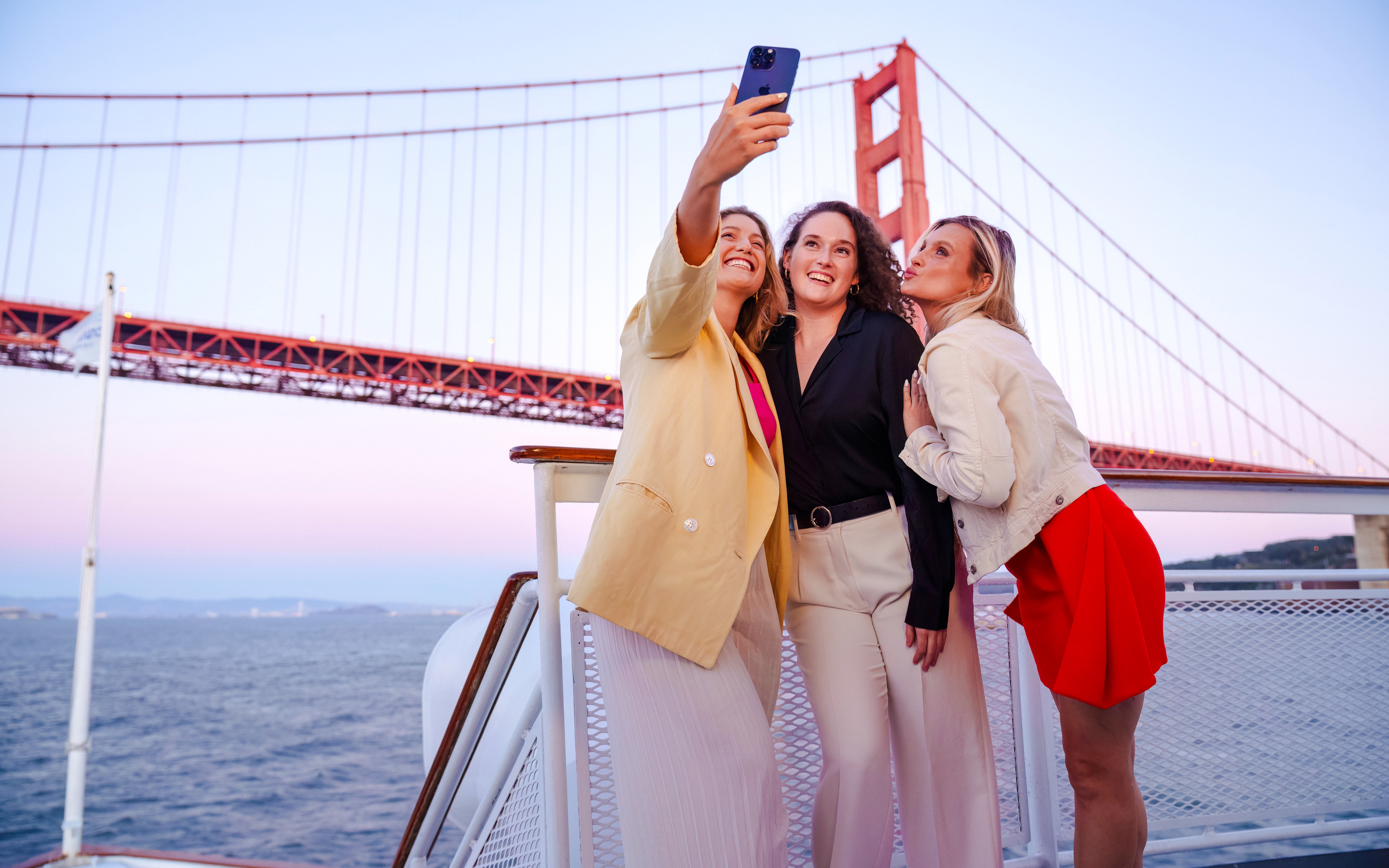 Friends taking a selfie on a San Francisco dinner cruise with Golden Gate Bridge in the background.