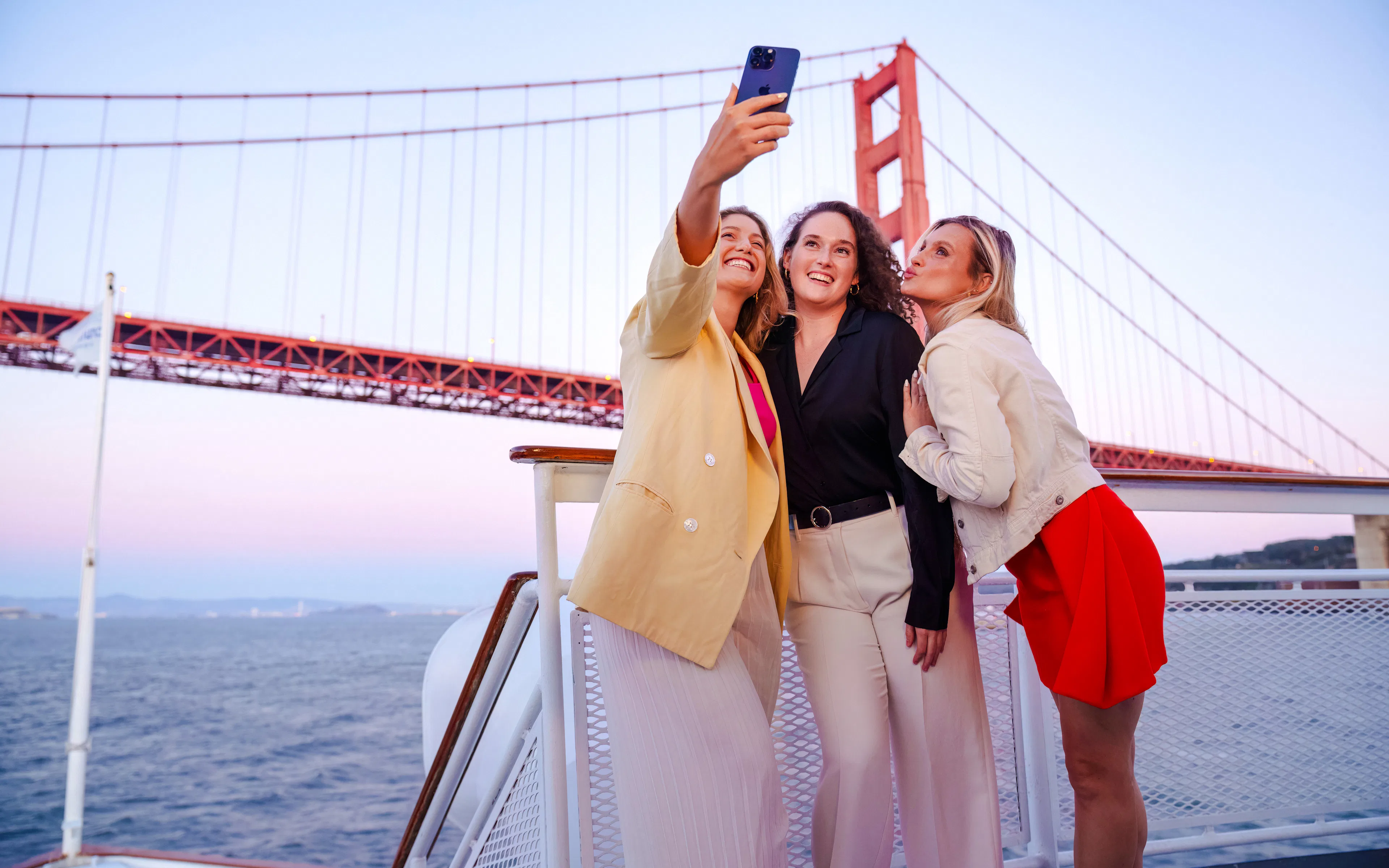 Friends taking a selfie on a San Francisco dinner cruise with Golden Gate Bridge in the background.