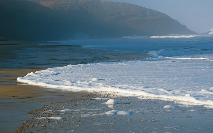 Legzira stone arches on the Atlantic Ocean coast, Morocco, with waves and sandy beach.