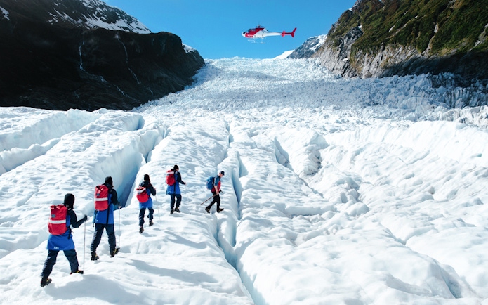Tourists hiking on Fox Glacier with a helicopter overhead, New Zealand.