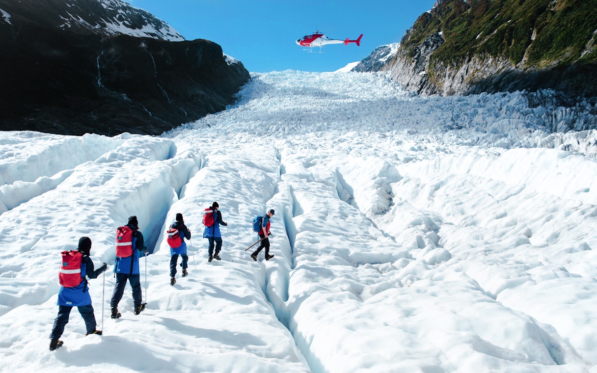 Tourists hiking on Fox Glacier with a helicopter overhead, New Zealand.