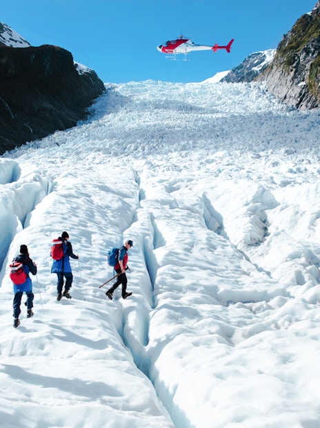 Tourists hiking on Fox Glacier with a helicopter overhead, New Zealand.