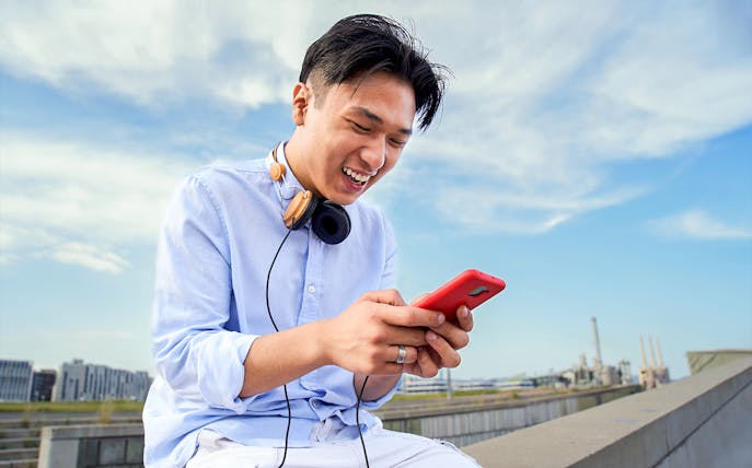 Man using smartphone outdoors with headphones, representing Korea Unlimited Data eSIM.