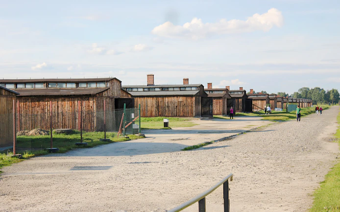 Auschwitz-Birkenau barracks with visitors walking along the gravel path.