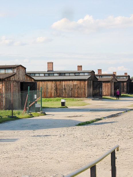 Auschwitz-Birkenau barracks with visitors walking along the gravel path.