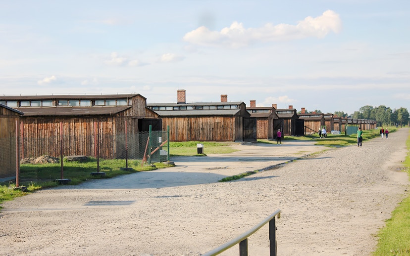 Auschwitz-Birkenau barracks with visitors walking along the gravel path.