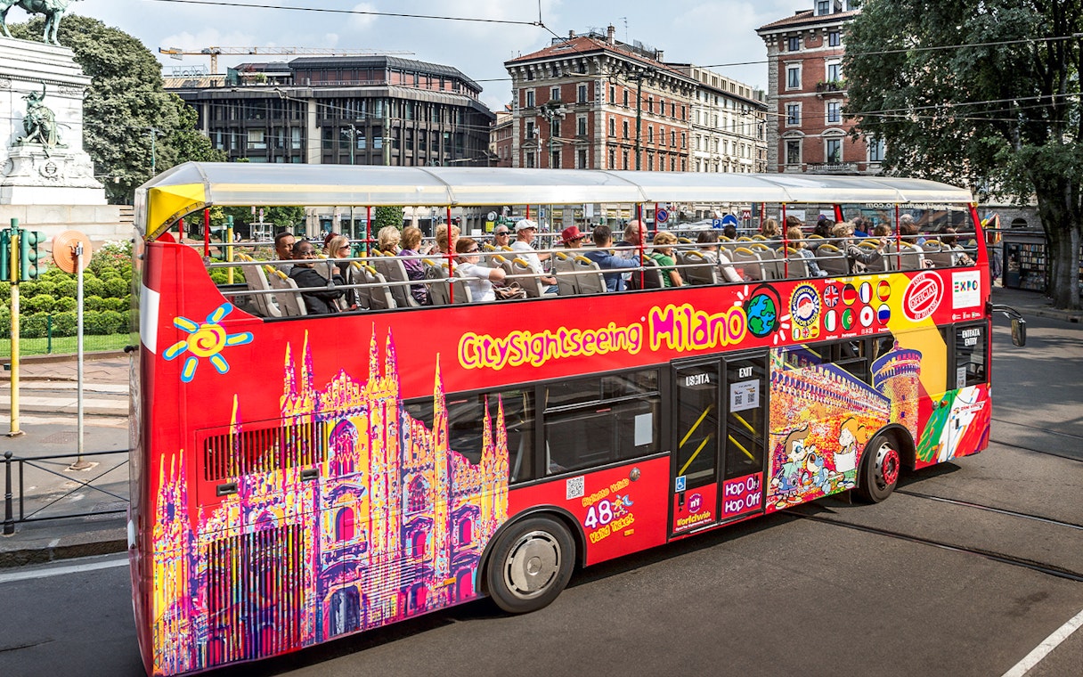 City Sightseeing bus with tourists in Milan near historical buildings.