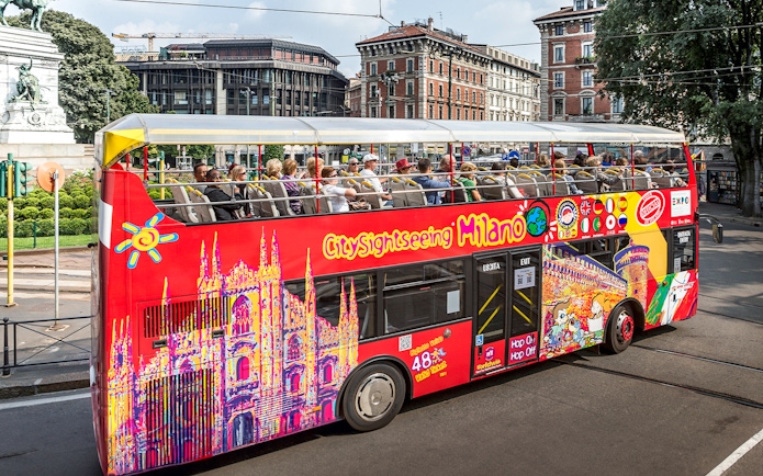 City Sightseeing bus with tourists in Milan near historical buildings.