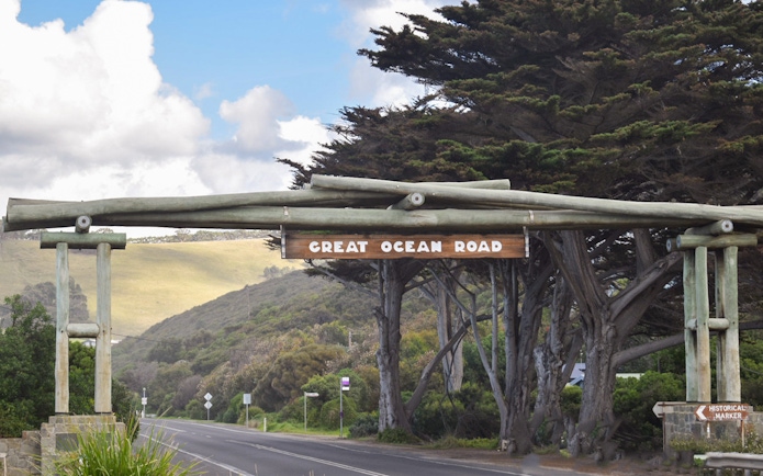 Great Ocean Road entrance sign with trees and road in Victoria, Australia.