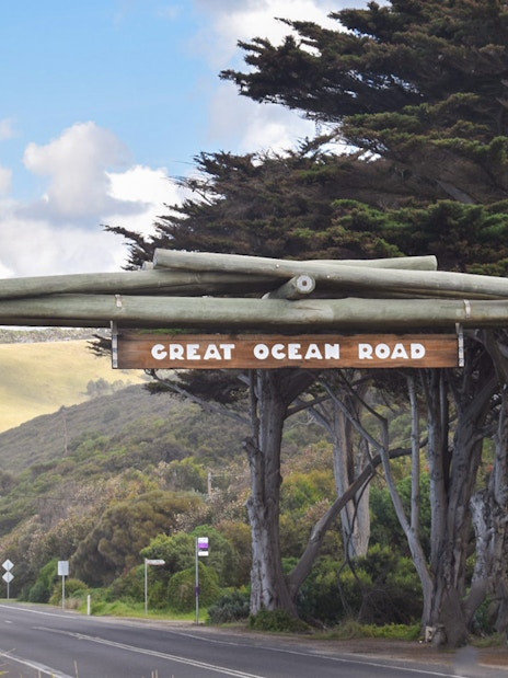 Great Ocean Road entrance sign with trees and road in Victoria, Australia.