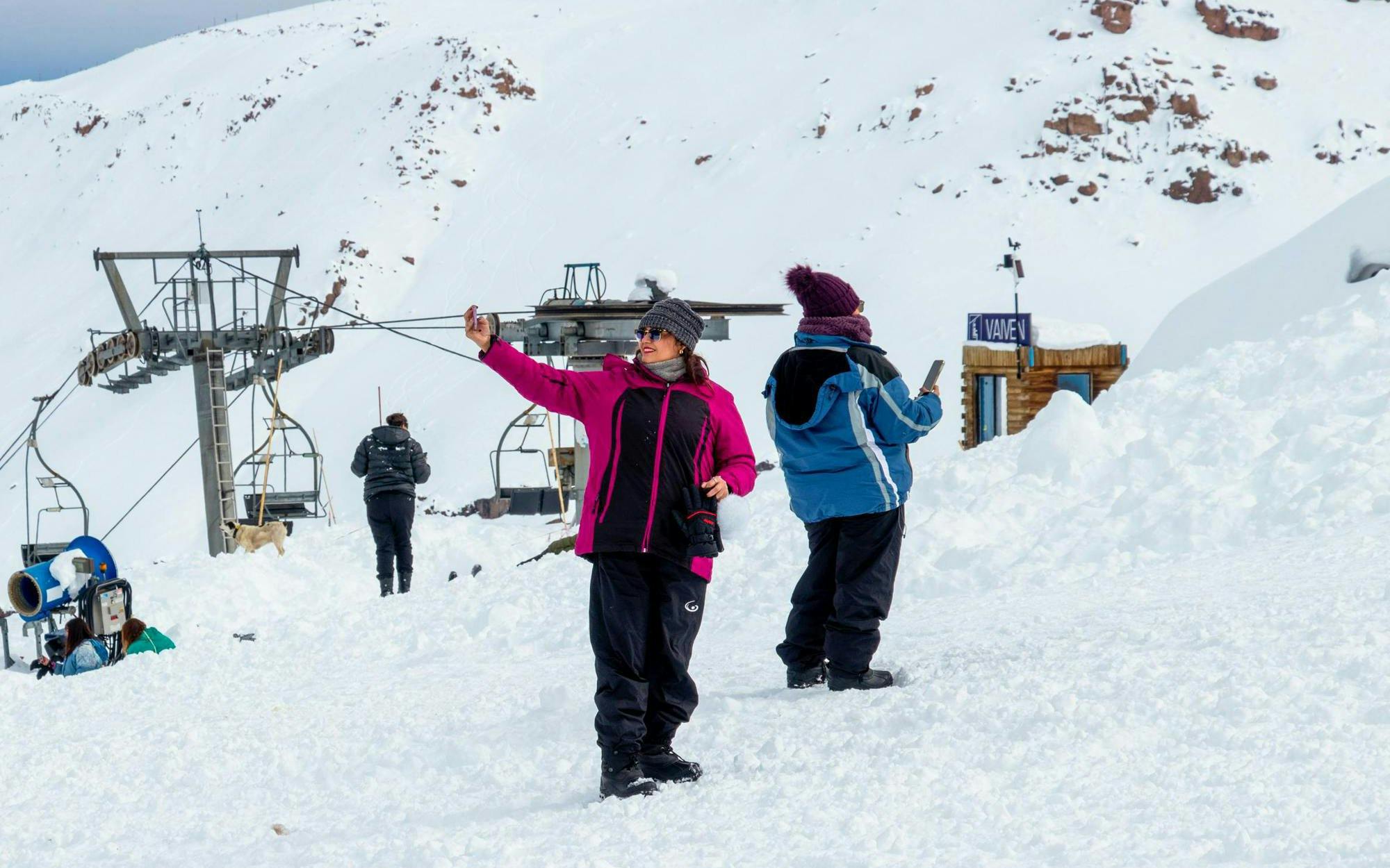 Tourists taking photos at Valle Nevado ski resort with snowy mountains and ski lift in background.