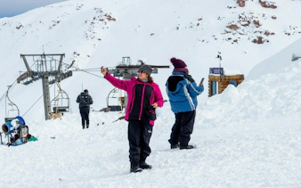 Tourists taking photos at Valle Nevado ski resort with snowy mountains and ski lift in background.