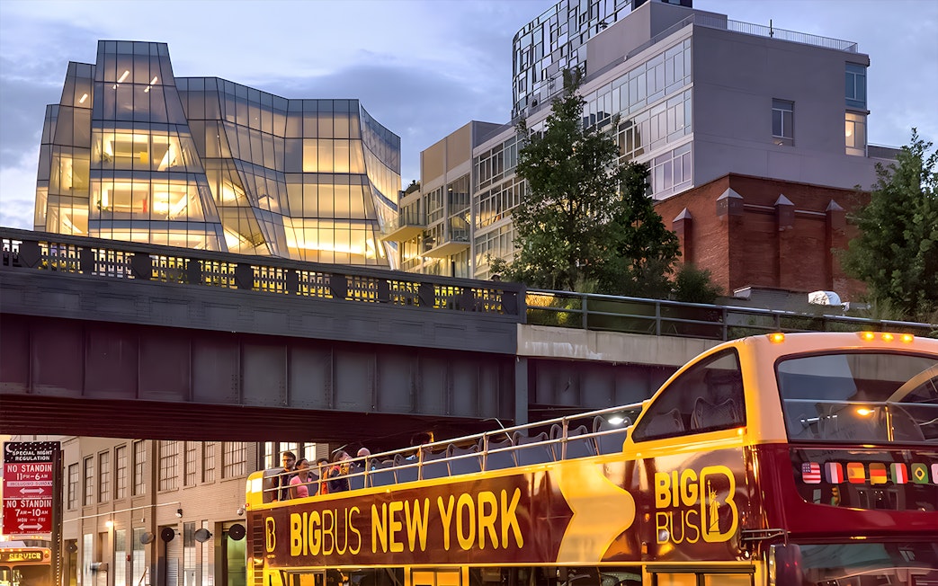 Big Bus New York night tour passing under illuminated modern architecture.