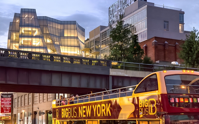 Big Bus New York night tour passing under illuminated modern architecture.