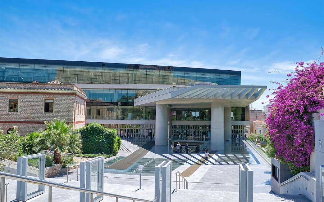 Acropolis Museum entrance in Athens, Greece, with modern architecture and vibrant bougainvillea.