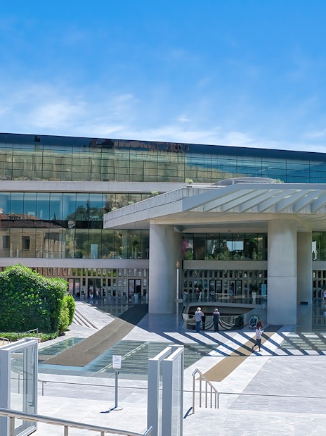 Acropolis Museum entrance in Athens, Greece, with modern architecture and vibrant bougainvillea.