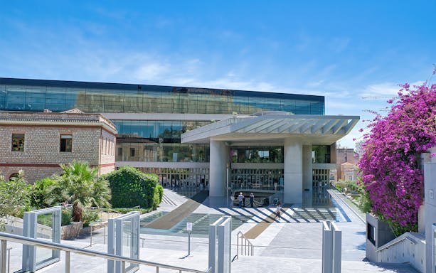 Acropolis Museum entrance in Athens, Greece, with modern architecture and vibrant bougainvillea.