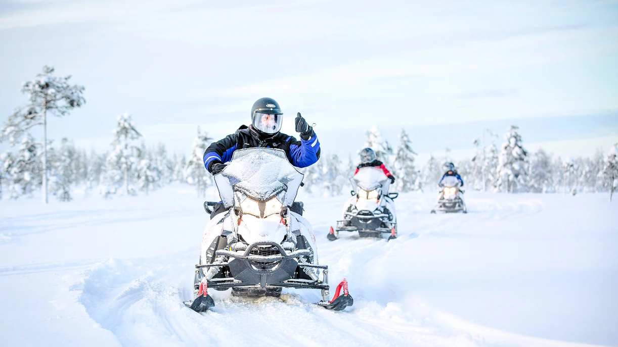 Snowmobile riders on a snowy trail in Rovaniemi, surrounded by snow-covered trees.