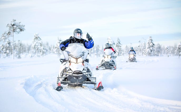 Snowmobile riders on a snowy trail in Rovaniemi, surrounded by snow-covered trees.