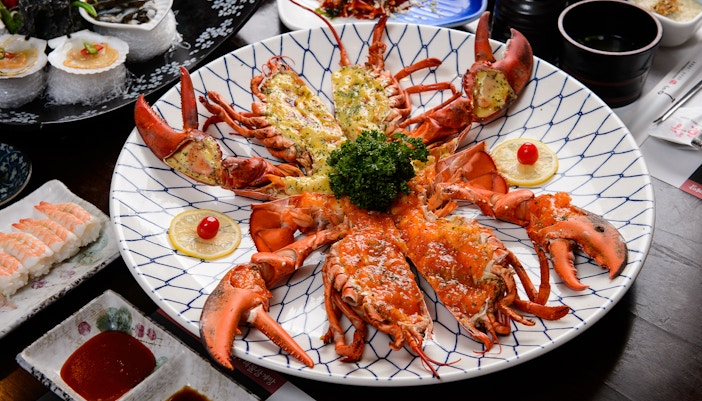 Lobster platter with lemon slices and garnish, surrounded by sushi and dipping sauces.