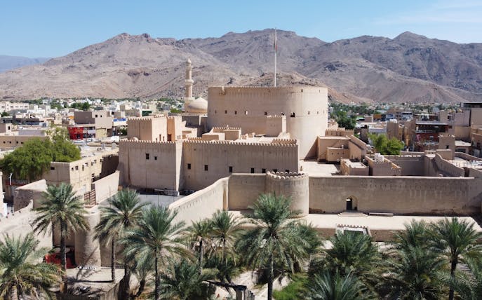 Nizwa Fort in Oman with surrounding palm trees and mountains in the background.