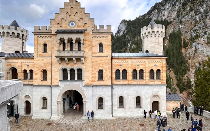 Courtyard view of Neuschwanstein Castle with visitors and mountain backdrop.